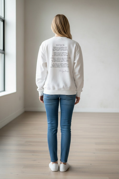 Woman wearing a white POETRY IN MOTION I AM I graphic sweatshirt with poetic black text on the back, paired with jeans